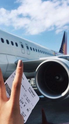 someone holding up their hand with a ticket in front of an airplane on the tarmac