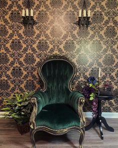 a green velvet chair sitting in front of a wallpapered wall with black and gold damask