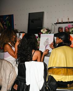 two women sitting next to each other at a table with paintings on the wall behind them