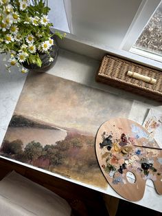 a painting is on the table next to a vase with flowers and paintbrushes