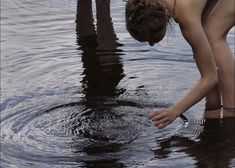 a woman bending over to touch the water