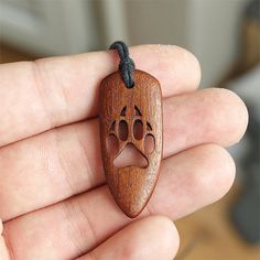 a hand holding a wooden pendant with a face drawn on it's front end