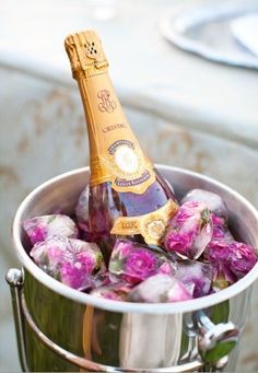 a bottle of champagne in a bucket filled with ice and pink flowers on a table