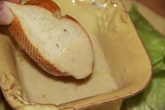 a close up of a person holding a piece of bread in a bowl with lettuce