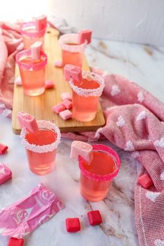 pink jellos are sitting on a wooden board with candy cubes around them