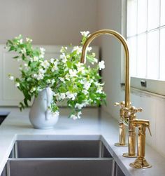 a kitchen sink sitting under a window next to a vase with white flowers in it