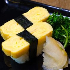 a black plate topped with sushi and broccoli