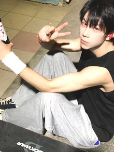 a young man sitting on the ground with his skateboard in front of him and pointing at something