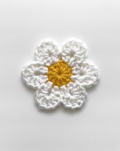 a crocheted white flower with yellow center sitting on top of a white surface