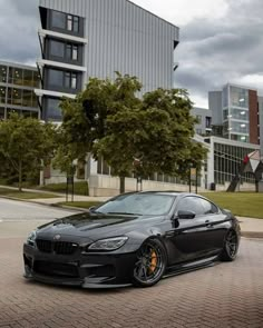 a black sports car parked in front of a building on a brick road next to trees