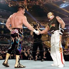 two men shaking hands in front of an audience at a wrestling match with one holding the other's hand