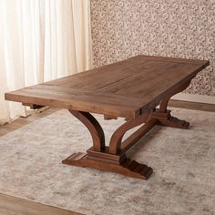 a wooden table sitting on top of a rug in front of a curtained window