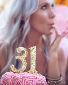 a woman blowing out the number thirteen candles on her birthday cake with pink frosting