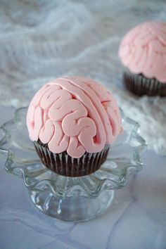 two cupcakes with pink frosting in the shape of a brain on top