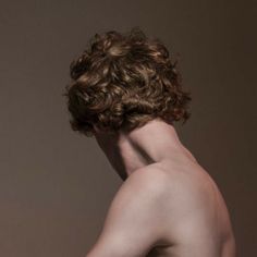 a naked man with no shirt on standing in front of a brown wall and looking back