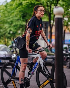 a woman with tattoos riding a bike down the street in front of a lamp post