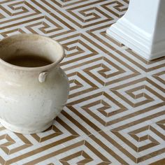 a white vase sitting on top of a brown and white tile floor next to a wall