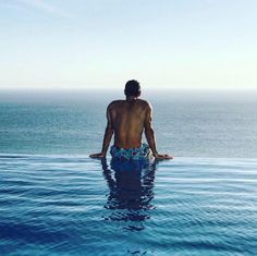 a man standing in the water with his back to the camera, facing the ocean