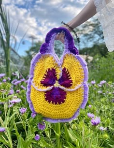 a crocheted bag with a flower on it is in the middle of some purple and yellow flowers