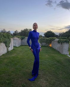 a woman in a blue dress standing on the grass with her hands on her hips