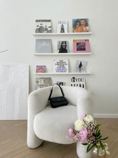 a white chair sitting in front of a wall filled with pictures and flowers next to a vase