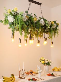 an arrangement of flowers hanging from the ceiling over a table with fruit and vegetables on it