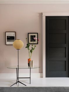 a living room with pink walls and black door, vases on glass table next to lamp