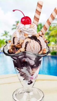 an ice cream sundae with cherries and nuts in a glass dish on a table next to a pool