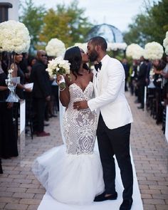 a bride and groom kissing in front of an outdoor ceremony with white flowers on the aisle