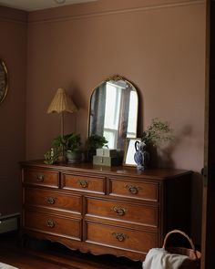 a dresser with a mirror and plants on it in a room that has brown walls