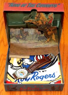 an open box with a watch inside on a wooden table next to a card game