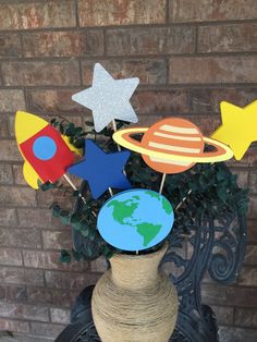 a vase filled with paper planets and stars sitting on top of a table next to a brick wall