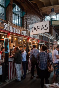 people standing in line to get food at a tapas restaurant on the street corner