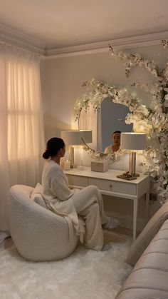 a woman sitting in front of a mirror on top of a white chair next to a table