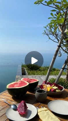 watermelon and other fruits on a wooden table with the ocean in the background