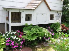 a white bird house surrounded by flowers and greenery