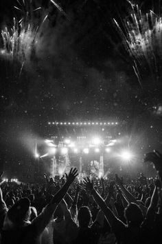 a crowd at a concert with their hands in the air as fireworks go off behind them