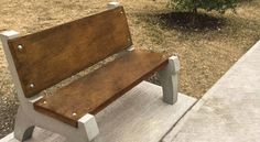 a wooden bench sitting on the side of a sidewalk next to a tree and bushes