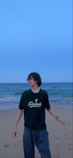 a young man standing on top of a sandy beach next to the ocean under a blue sky