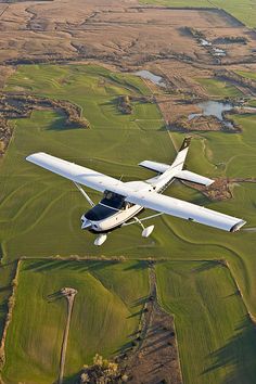 an aerial view of a small plane flying in the sky over green fields and farmlands