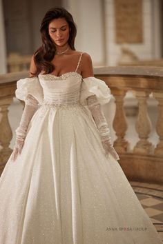 a woman in a white wedding dress with long sleeves and pearls on the shoulders is standing near a staircase