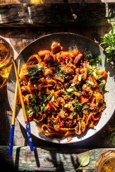 a plate of pasta with meat and vegetables next to two glasses of beer on a wooden table