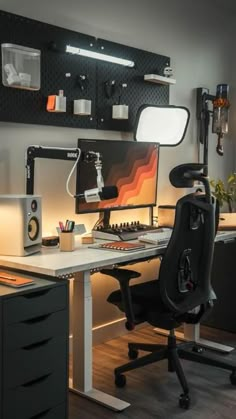 a desk with a monitor, keyboard and speakers on it in front of a wall mounted light