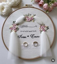 a white embroidered wedding ring and veil with pink flowers on the hoop next to it