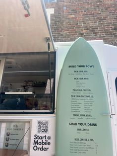 the surfboard is leaning up against the building's exterior wall, which also displays information about how to order