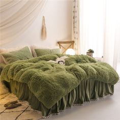 the bed is made up with fluffy green blankets and pillows on it's headboard