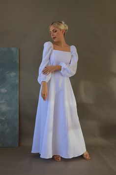 a woman in a white dress standing next to a painting