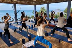 a group of people doing yoga on mats in front of the ocean with their hands up