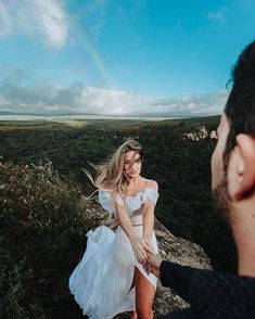 a woman in a white dress standing on top of a hill next to a man