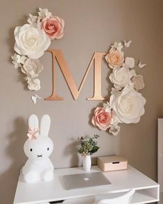 a white desk topped with a laptop computer next to a pink flower wall letter m